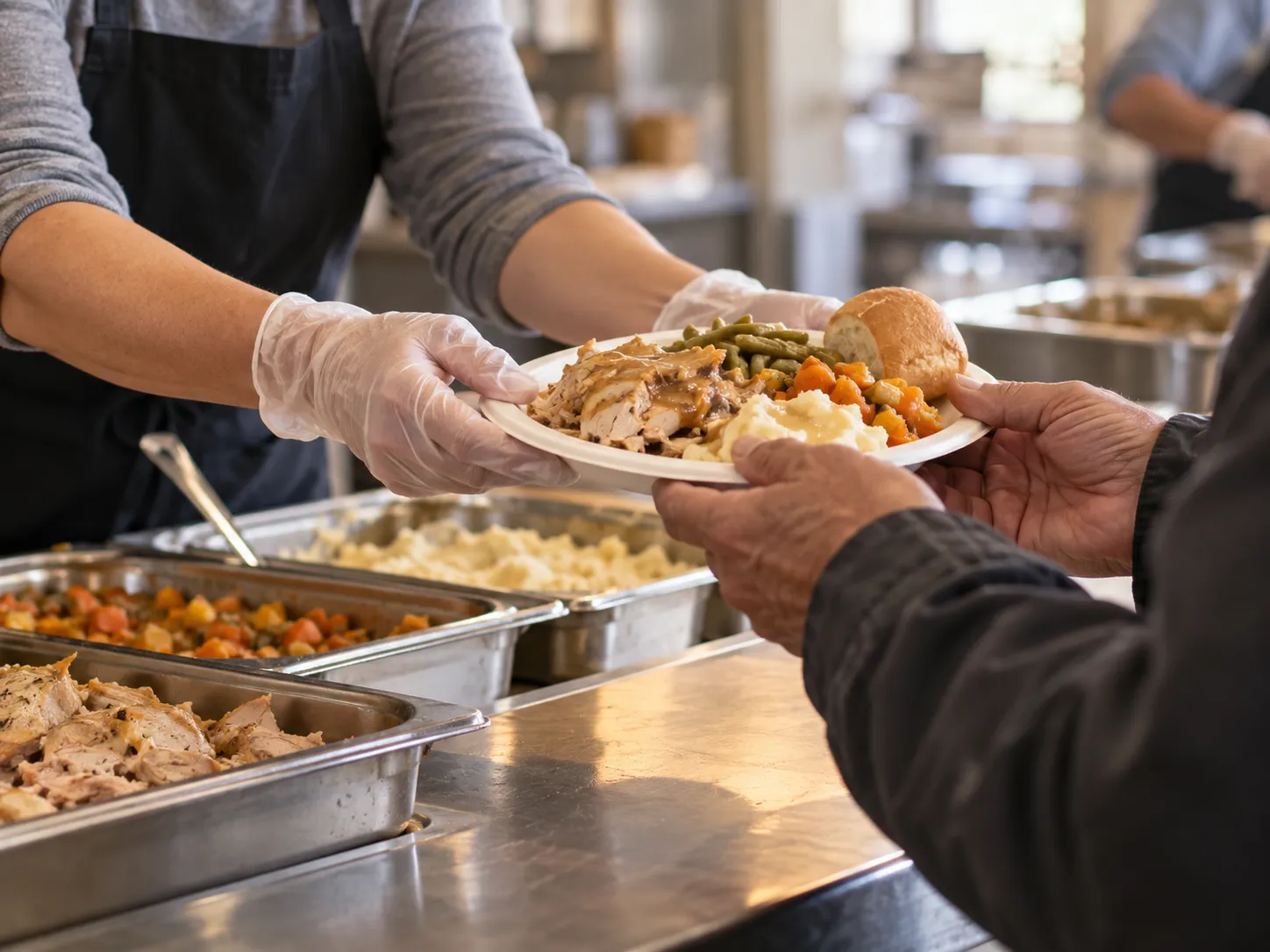 A volunteer in gloves hands a plated meal to a guest across a rescue mission serving line