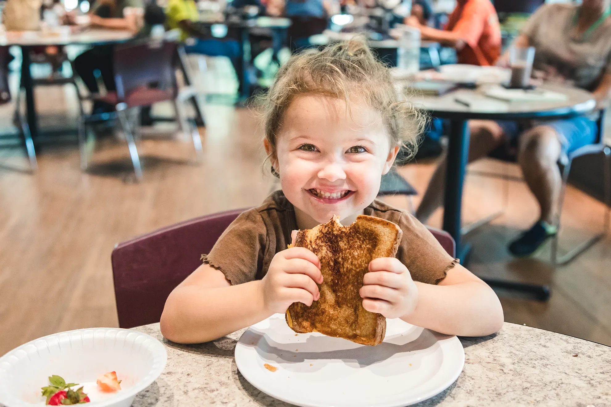 A young girl smiles over a grilled cheese sandwich in the Orange County Rescue Mission dining room